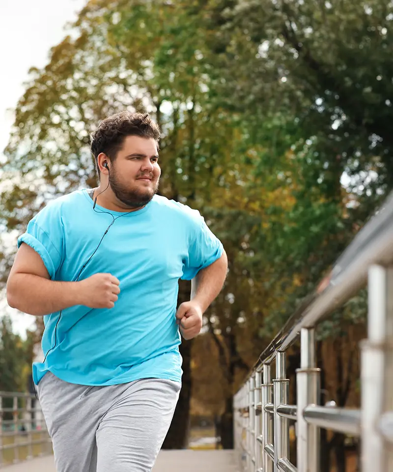 Overweight man jogging outdoors, embracing a healthier lifestyle. Showcasing the journey to improved fitness and self-confidence through consistent movement and mindset changes. A visual representation of sustainable health habits. 2024. Mark Ludlow – The Life Changing Health Coach.